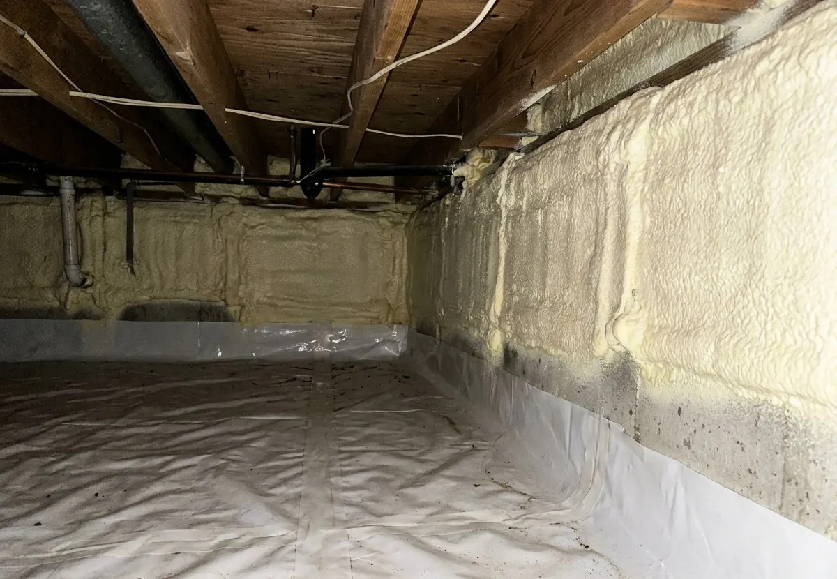 Crawl space foundation walls insulated with spray foam and a white vapor barrier